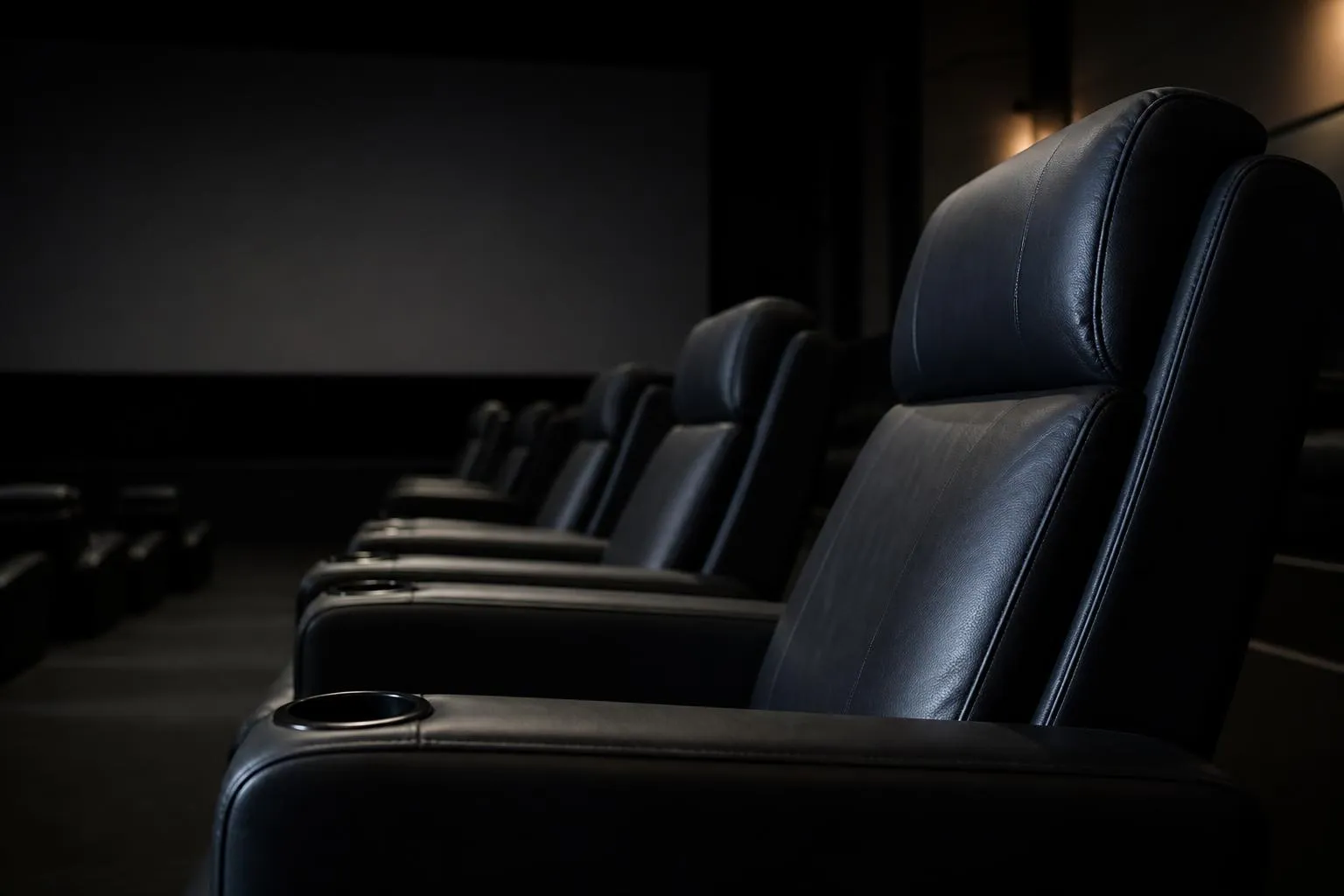 Une rangée de fauteuils de cinéma inclinables, vides, face à un écran plongé dans le noir